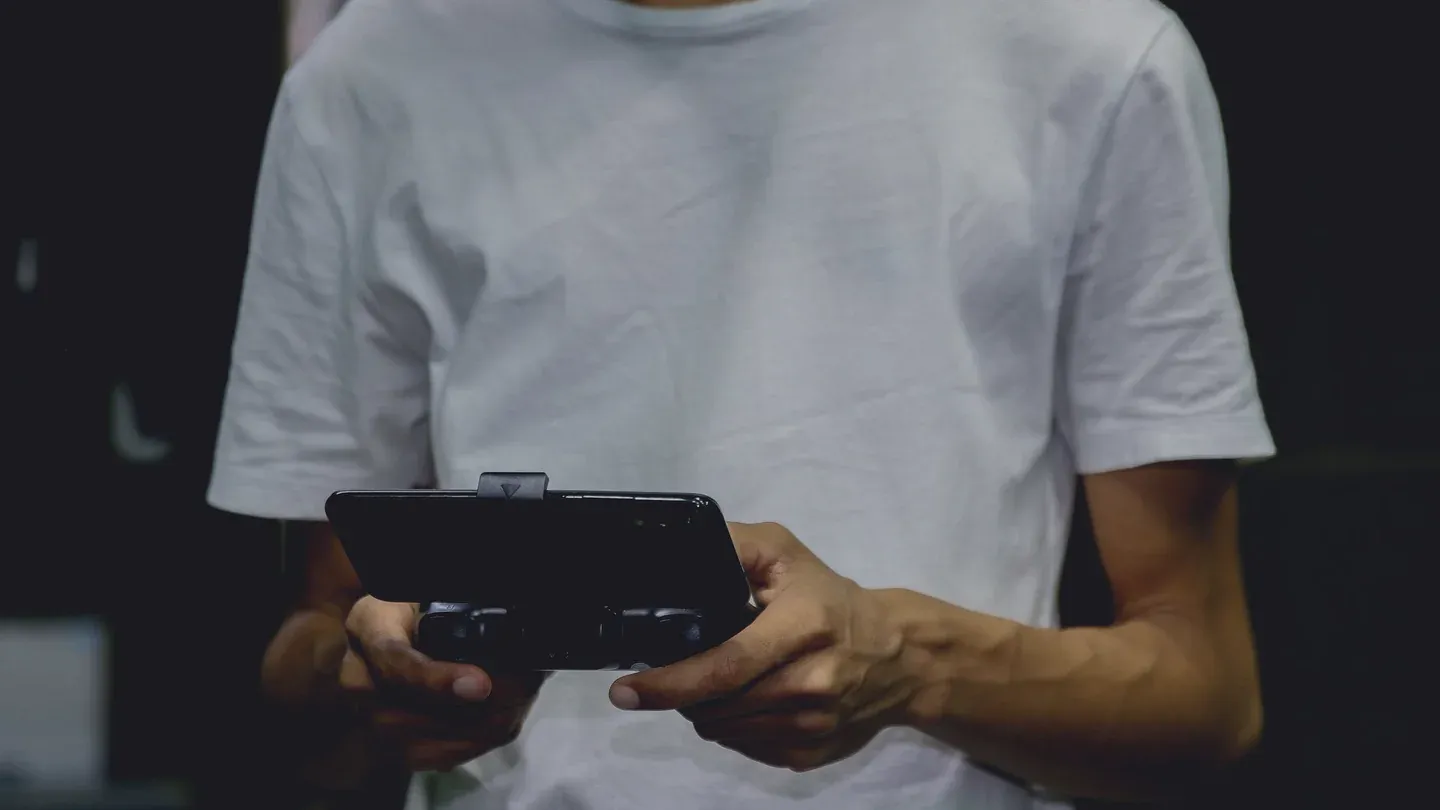 A person holding a physical game controller with a smartphone mounted above it