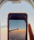 A traveler holding a smartphone in front of an airplane window with the wing visible