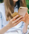 A person sitting outdoors holding a smartphone in one hand and a payment card in the other
