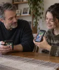 A parent and adult daughter compare the same fictional puzzle game on separate phones at home
