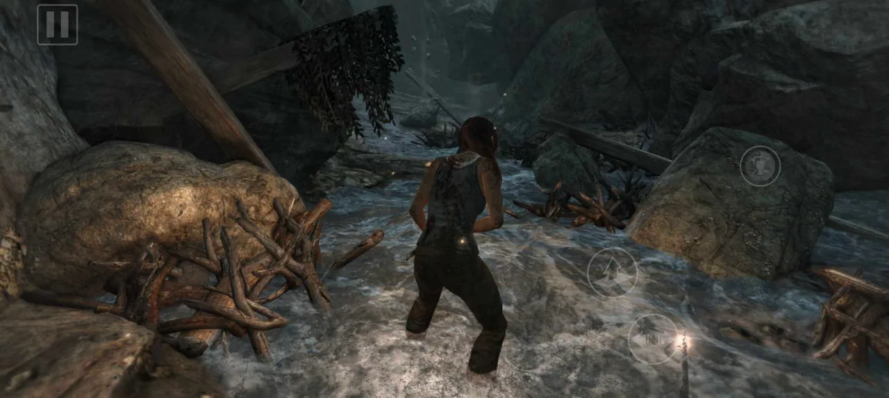 Lara Croft wades through a rocky stream with translucent mobile controls on screen
